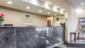 A hotel reception area with a marble counter, a framed certificate, and a small table with a vase of flowers.