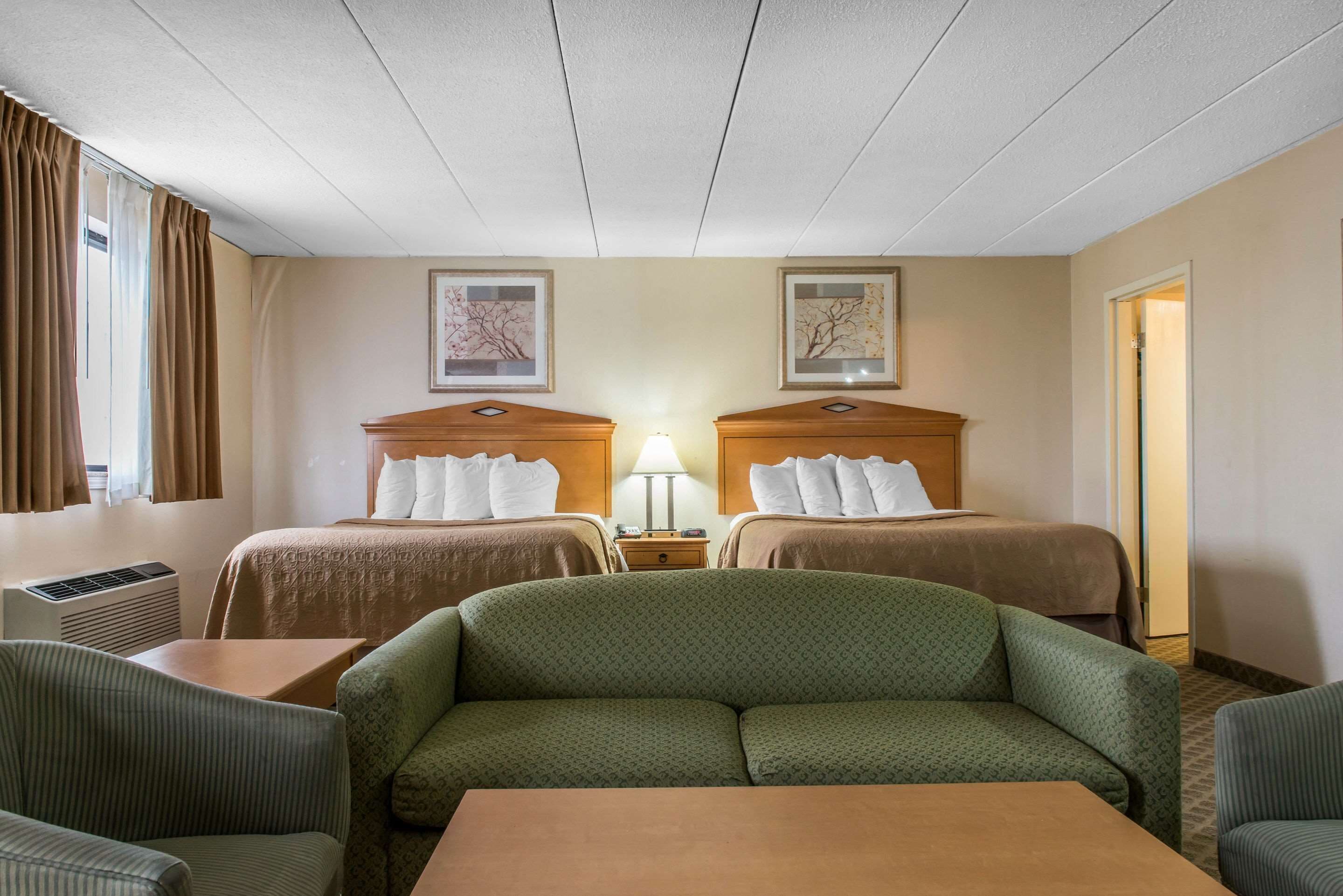 A hotel room with two beds, a sofa, a table, and a lamp.
