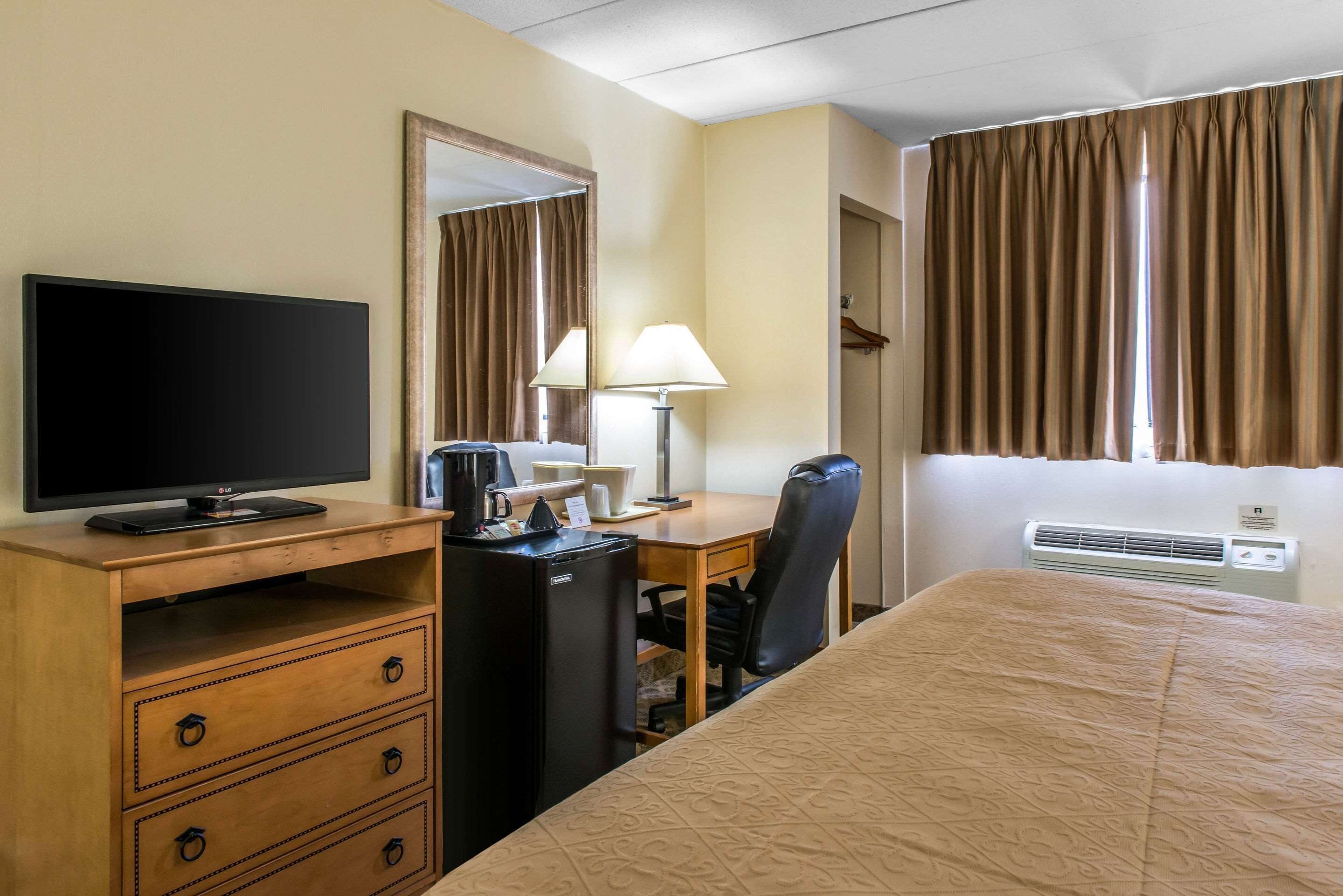 Una habitación de hotel con una cama, un escritorio con ordenador, televisor, lámpara y calefactor.