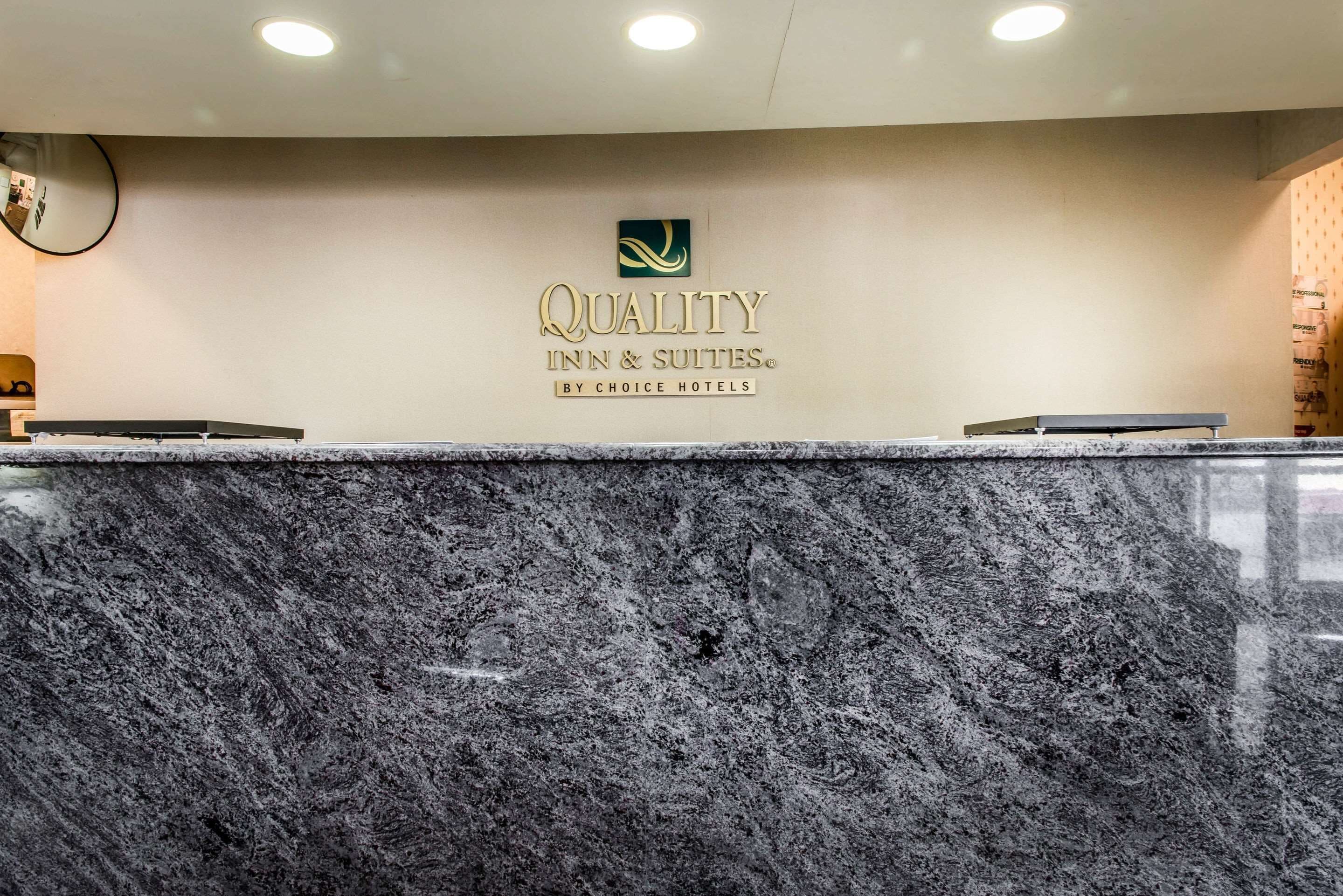 Un comptoir d’accueil avec un plateau en marbre et, sur le mur qui le surplombe, le logo de « Quality Inn & Suites by Choice Hotels ».