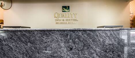 Een receptiebalie met een marmeren blad en een logo voor 'Quality Inn & Suites by Choice Hotels' op de achtergrond.