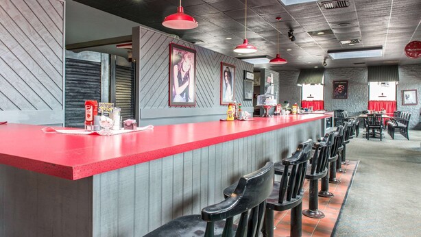 A bar area with a red counter, black bar stools, and framed pictures on the wall.