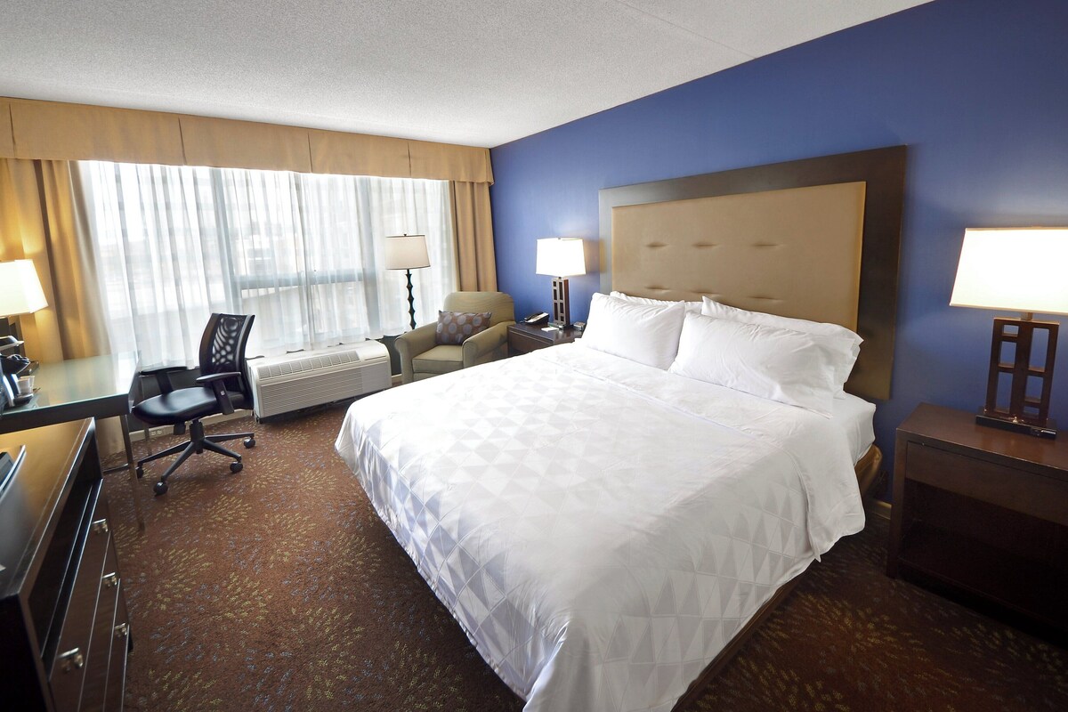 A hotel room with a large bed, a desk with a computer, a chair, and a TV.