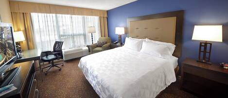 A hotel room with a large bed, a desk with a computer, a chair, and a TV.