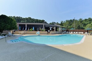 A swimming pool with lounge chairs and umbrellas, surrounded by a building with a covered patio area. - Holiday Inn Washington DC-Greenbelt MD by IHG (Greenbelt)