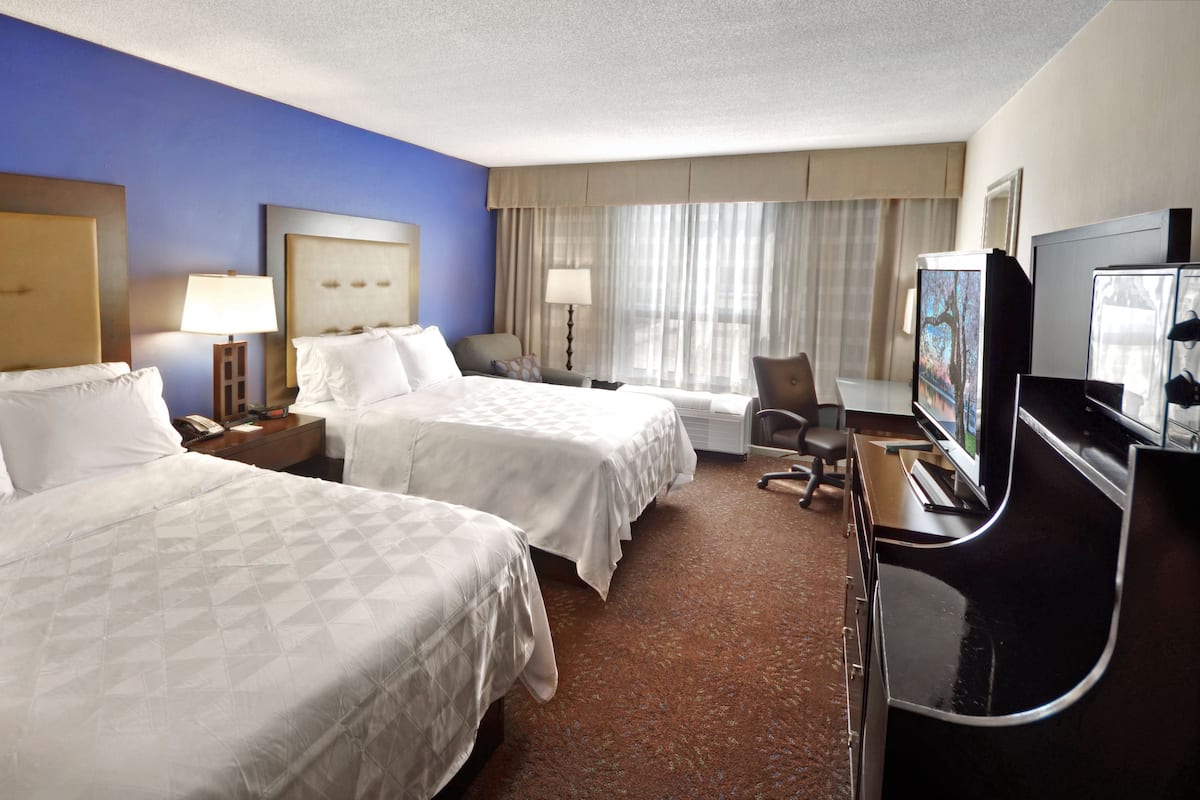 A hotel room with two beds, a desk with a TV, a chair, and a window with curtains.