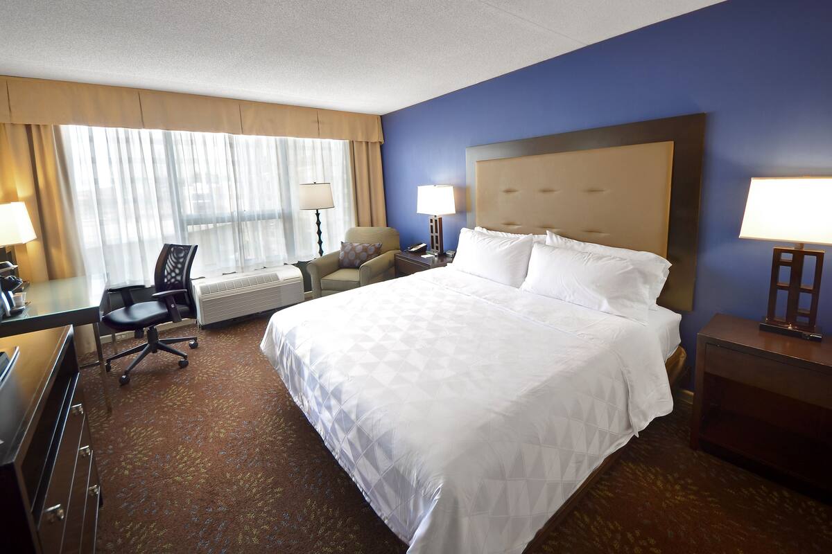 A hotel room with a large bed, a desk with a chair, a television, and a desk lamp.