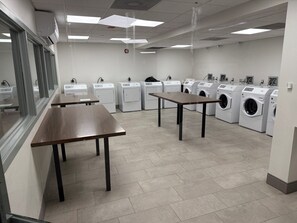 A laundry facility with multiple washing machines, tables, and a tiled floor. - Holiday Inn Washington DC-Greenbelt MD by IHG (Greenbelt)