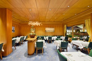 A dining area with wooden paneling, green upholstered chairs, and white tablecloths.