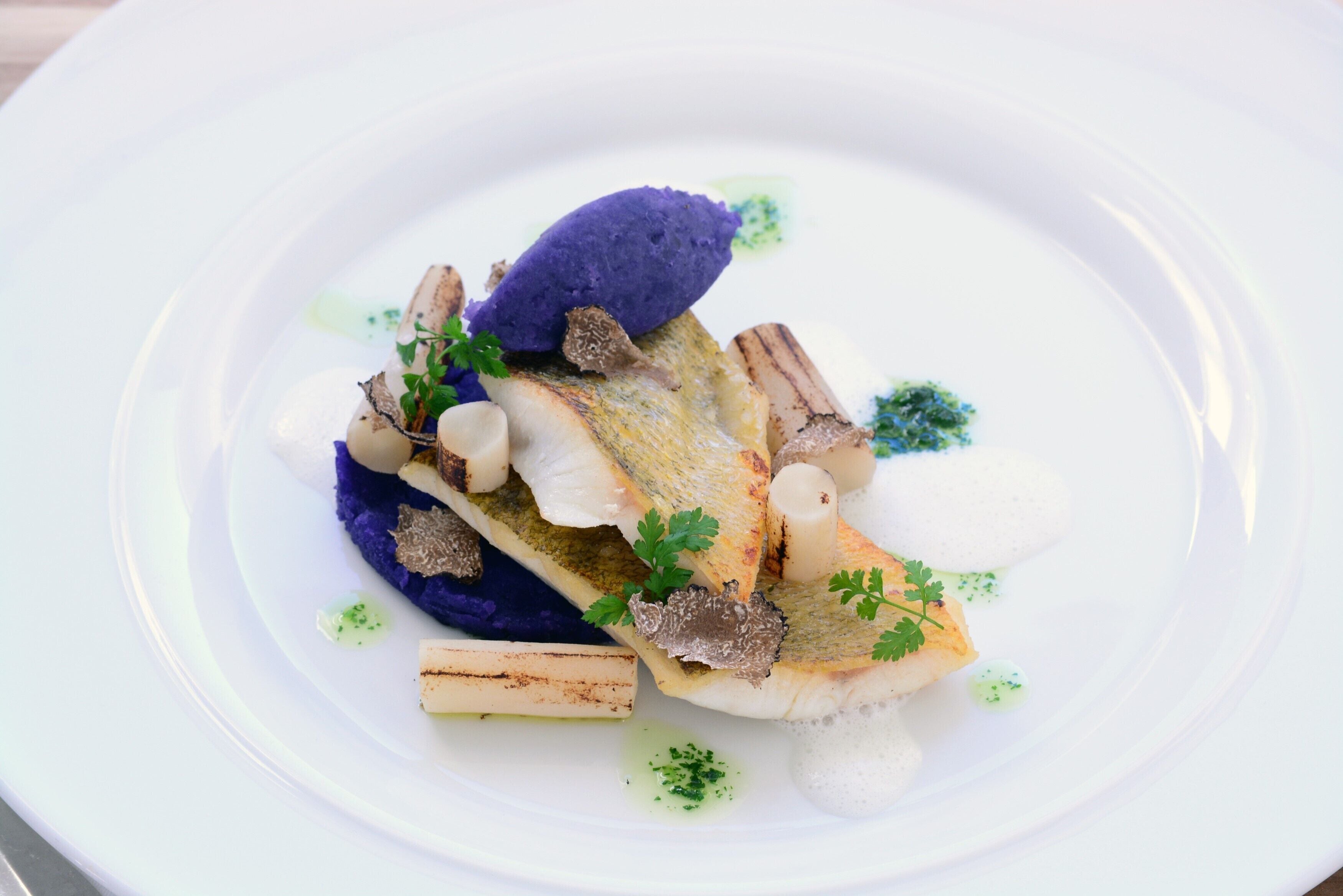 Un plato blanco con un guiso de pescado, detalles morados y adornos verdes.