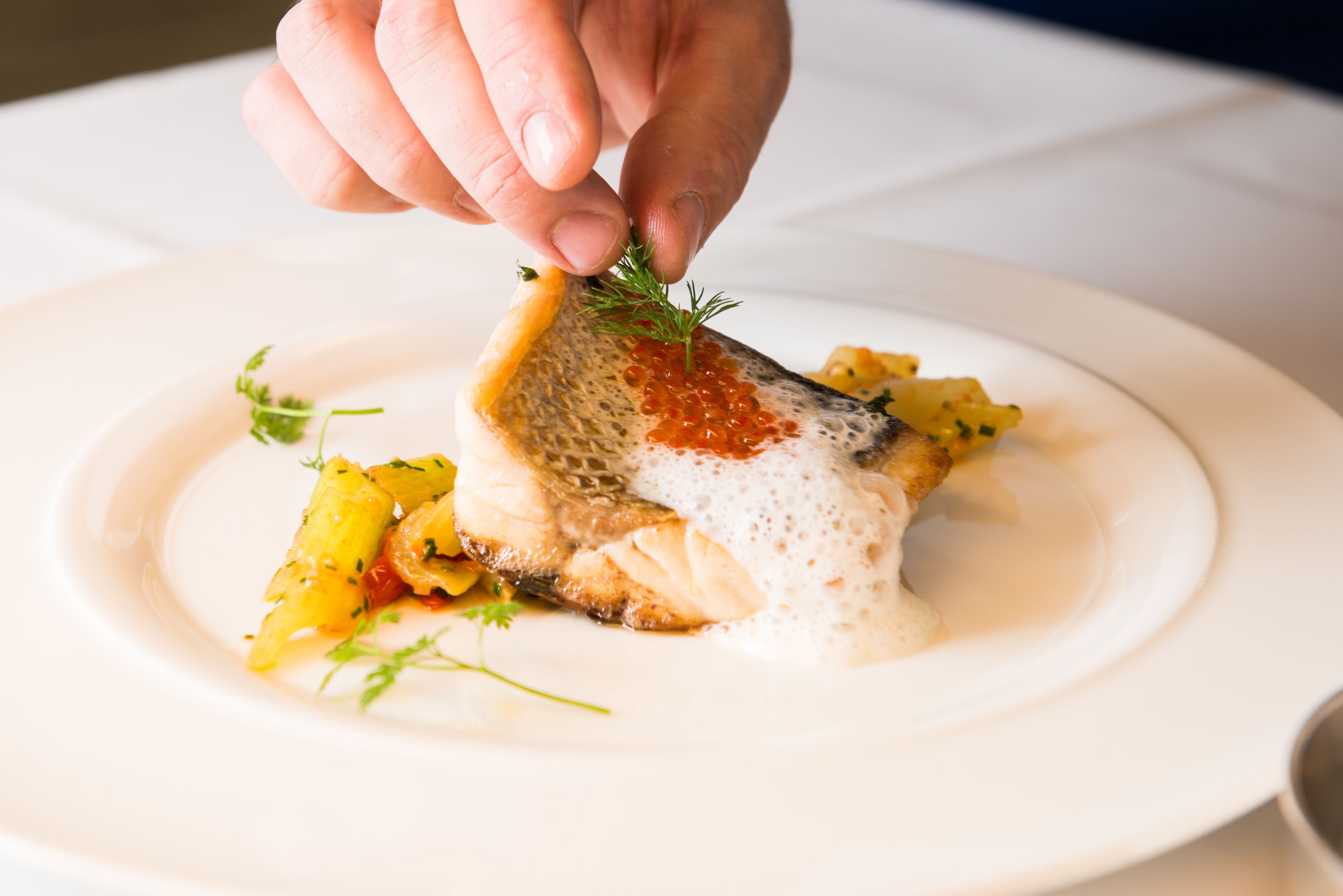 Un plato con un filete de pescado cubierto de caviar rojo y adorno de eneldo.