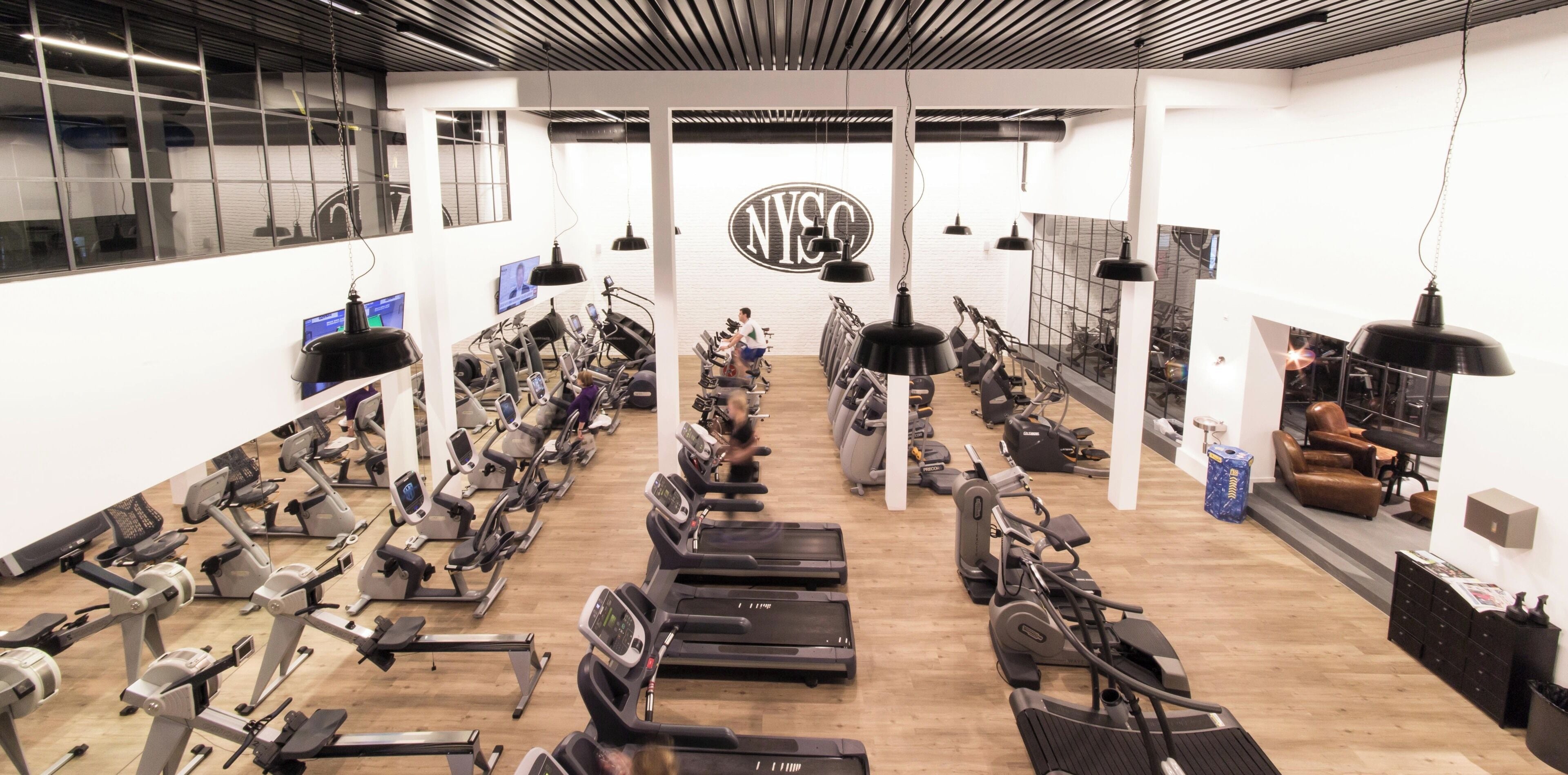 Ein Fitnessraum mit Laufbändern, Ergometer und Crosstrainern, die in Reihen angeordnet sind.
