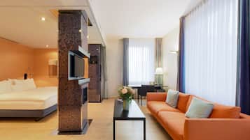 Ein Hotelzimmer mit Bett, Sofa, Fernseher, Schreibtisch und einem fensterbepflanzten Fenster.