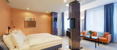 A modern hotel room with a large bed, a sofa, a coffee table, and a TV.