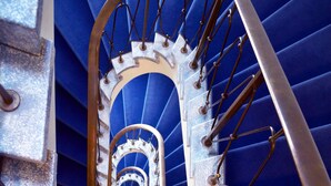 A spiral staircase with metal railings and a blue background. - Glärnischhof by Trinity (Zürich)