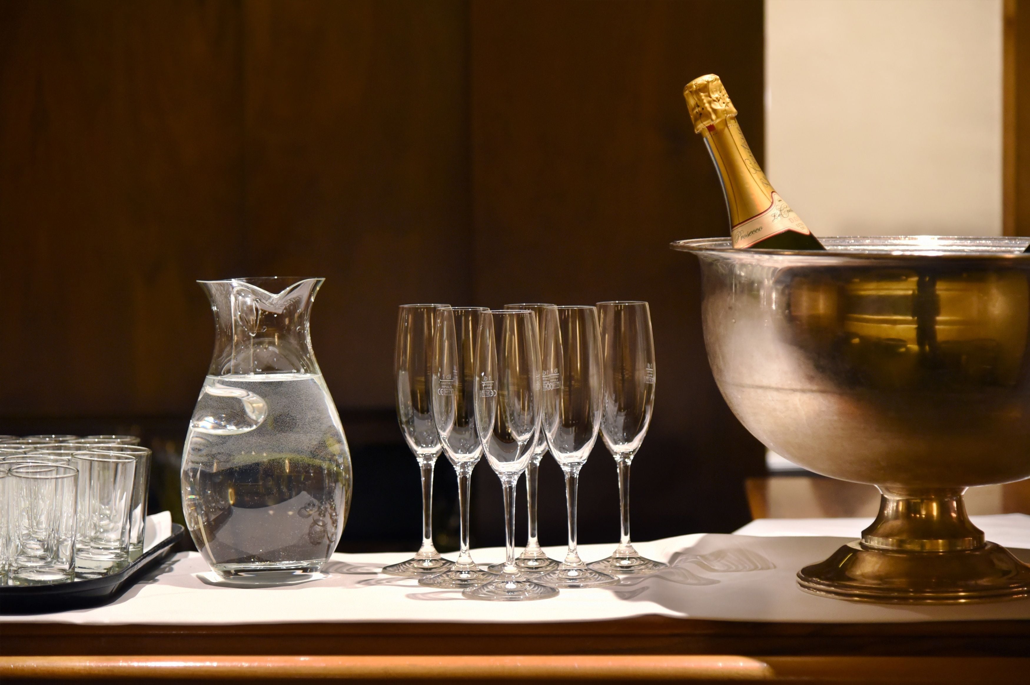 A table with a champagne bottle in a metal bucket, a pitcher, and several glasses.