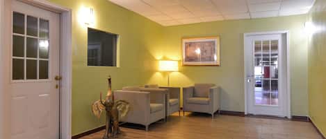 Una habitación con una puerta, dos sillones, una lámpara, un cuadro enmarco y un objeto decorativo.