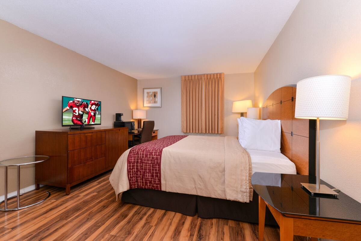 A hotel room with a bed, a TV, a desk, and a chair.