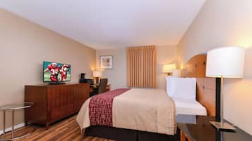 A hotel room with a bed, a desk, a television, a chair, a lamp, and a picture on the wall.