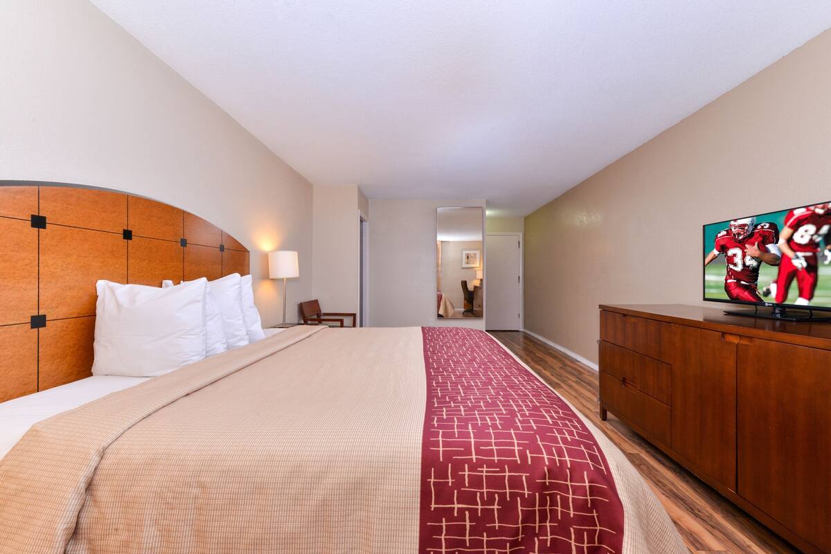 A hotel room with a bed, a TV, a wooden headboard, a red carpet, and a wooden dresser.