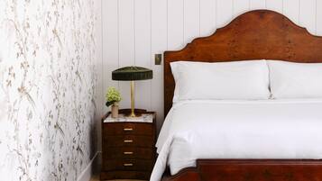 A neatly made bed with white linens, a wooden headboard, and a nightstand with a lamp and a small vase with flowers.