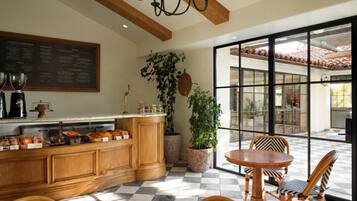 A breakfast bar with coffee and pastries, a dining area with chairs, and a large window with a view.