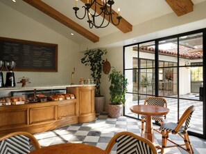 A breakfast bar with coffee and pastries, a dining area with chairs, and a large window with a view. - Inn At Rancho Santa Fe (Rancho Santa Fe)