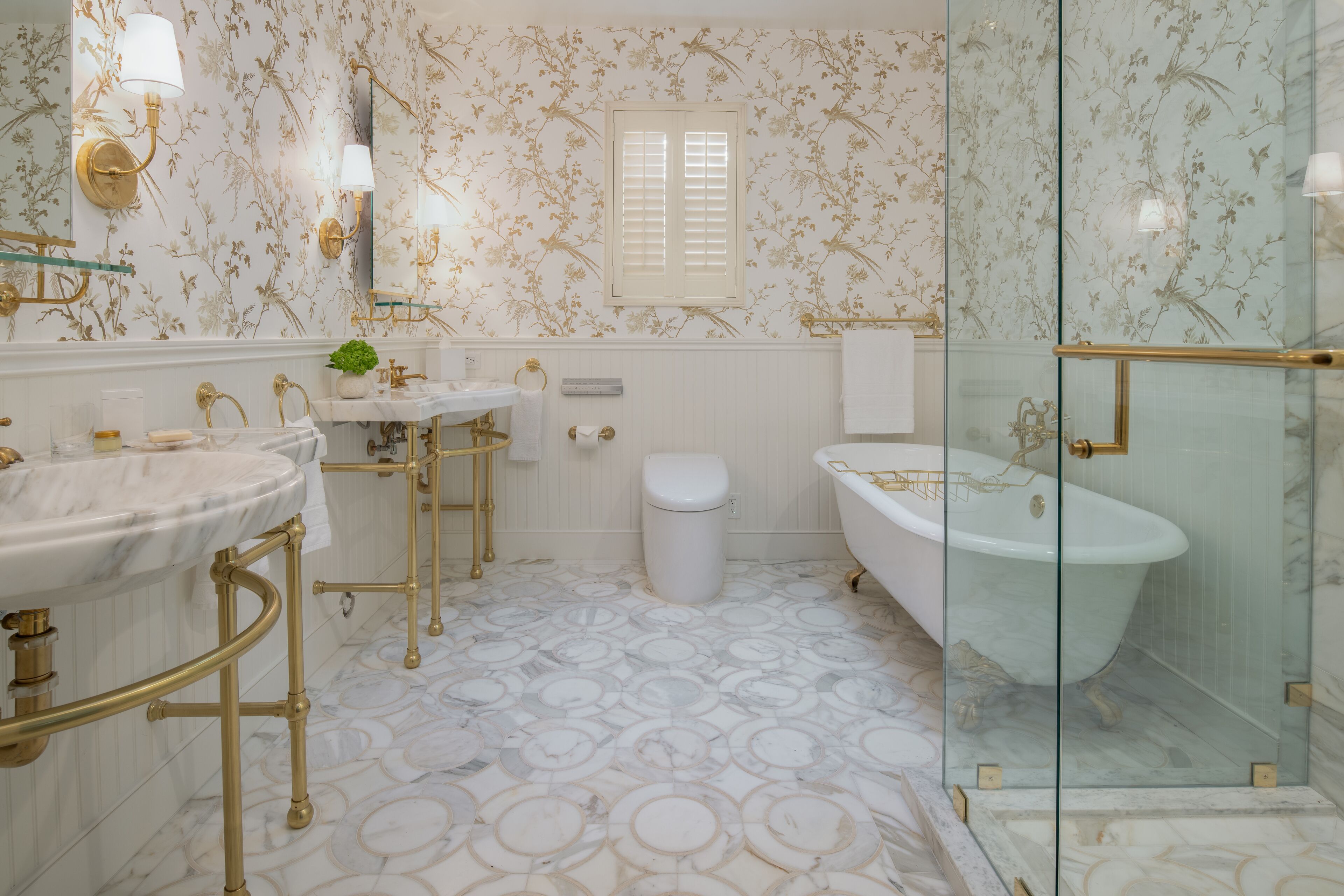 A bathroom with a marble floor, gold fixtures, a freestanding bathtub, and a glass-enclosed shower.