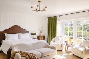 A bedroom with a large bed, two armchairs, a small table, and a window with curtains. - Inn At Rancho Santa Fe (Rancho Santa Fe)