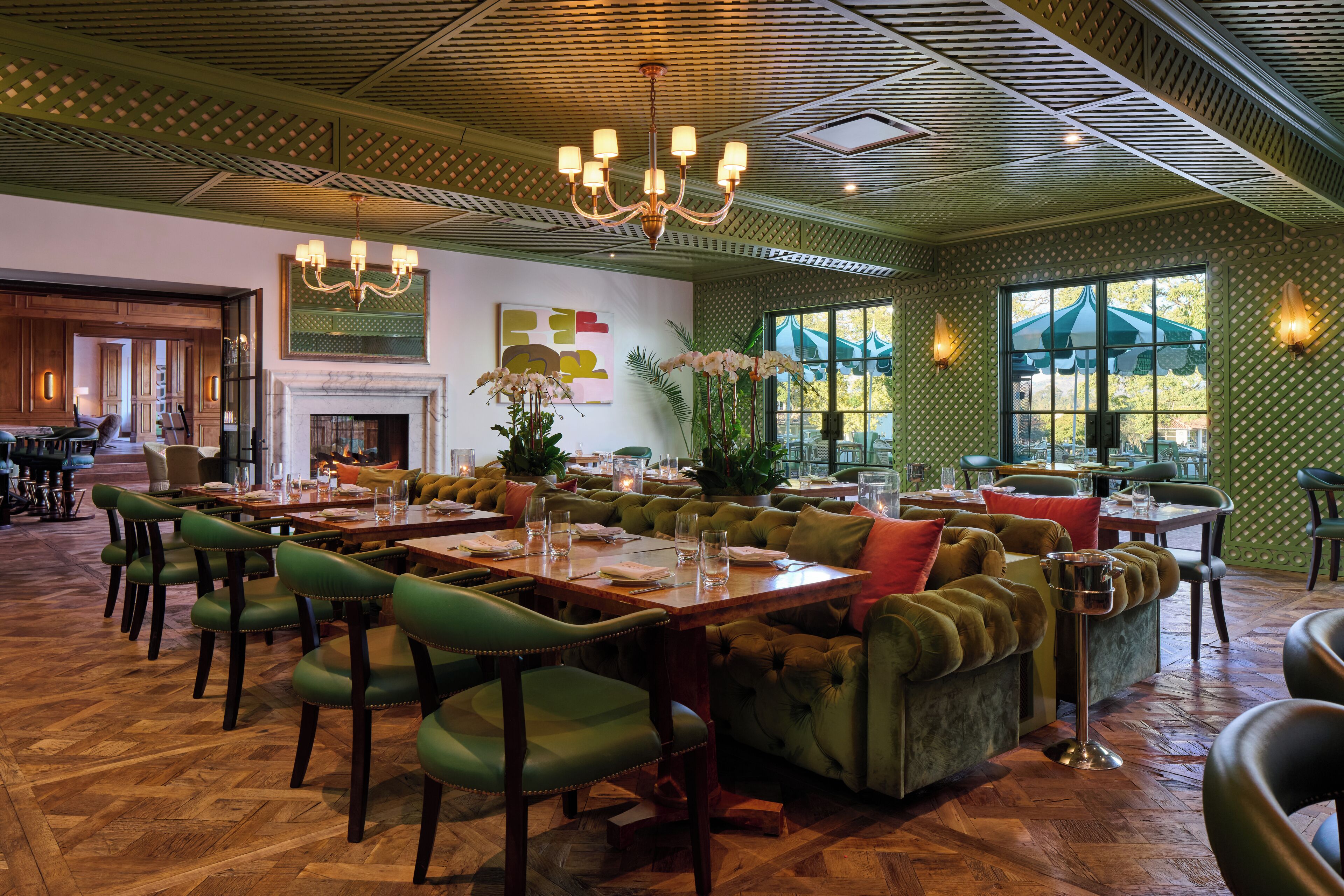 A restaurant with green upholstered seating, wooden tables, and a chandelier.