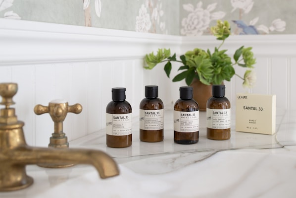 Un tocador de baño con cuatro botellas de loción corporal Santal 33 y una caja del mismo producto.