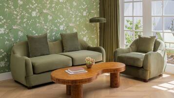 A living room with a green sofa, a matching armchair, and a wooden coffee table with a book and flowers.