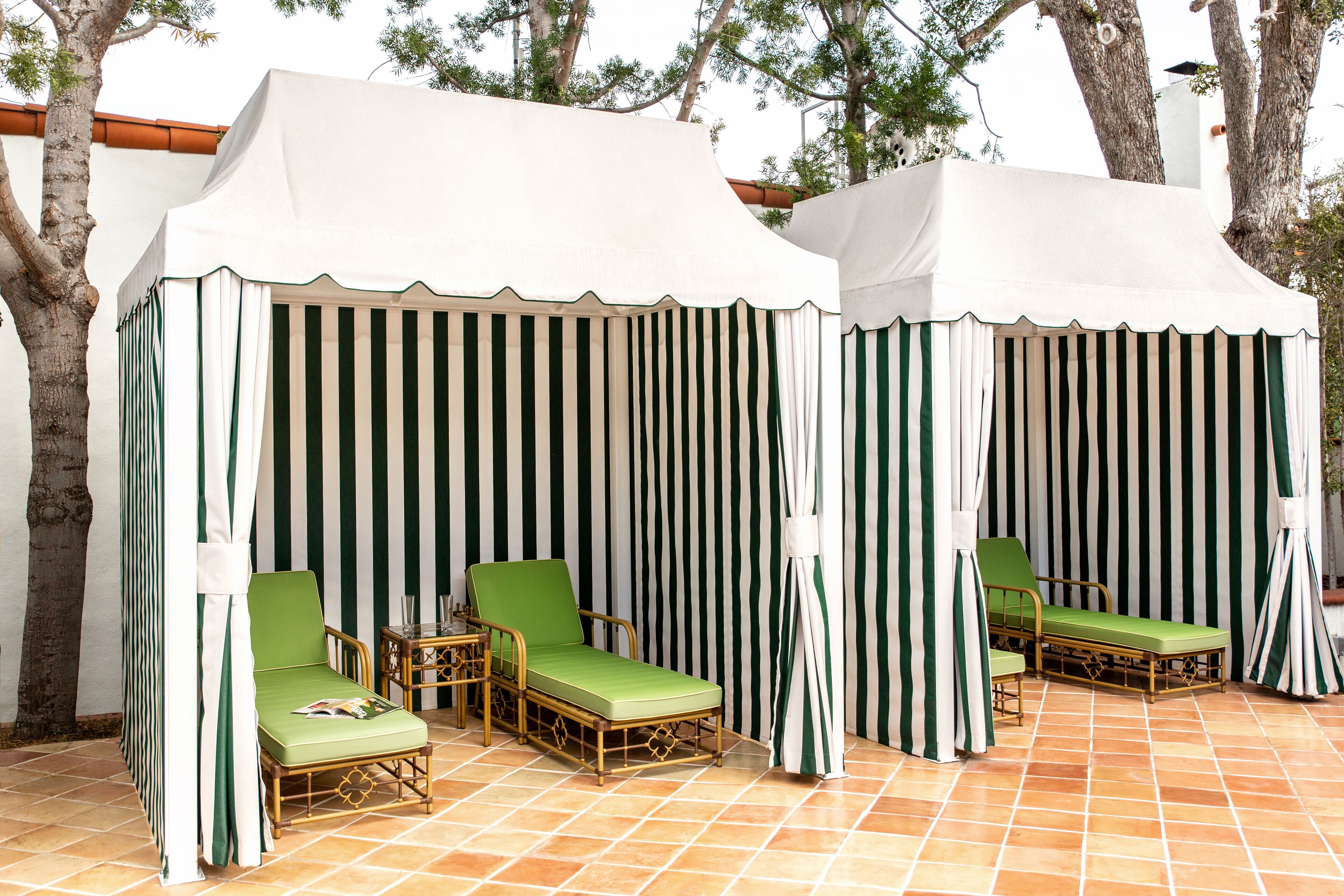 A covered outdoor seating area with striped curtains and green cushioned chairs.