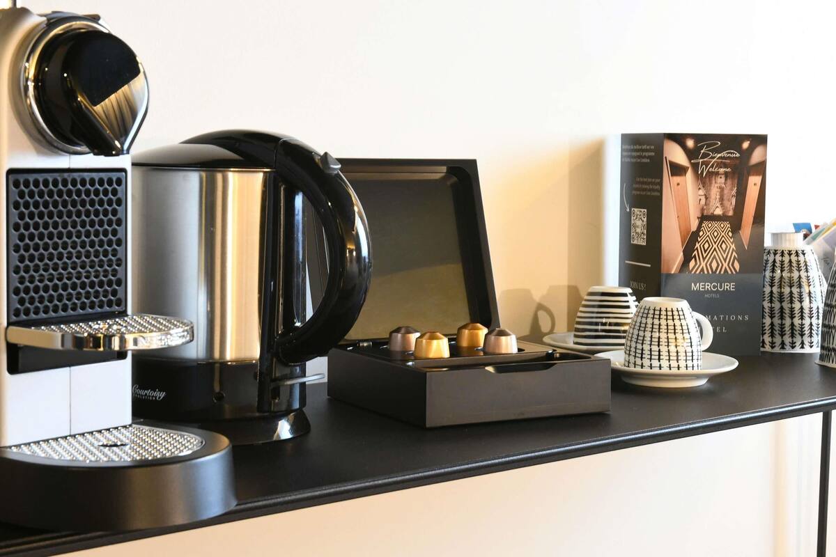 A coffee station with a coffee maker, a kettle, and a tray of pastries. There is a framed welcome sign and a stack of plates.