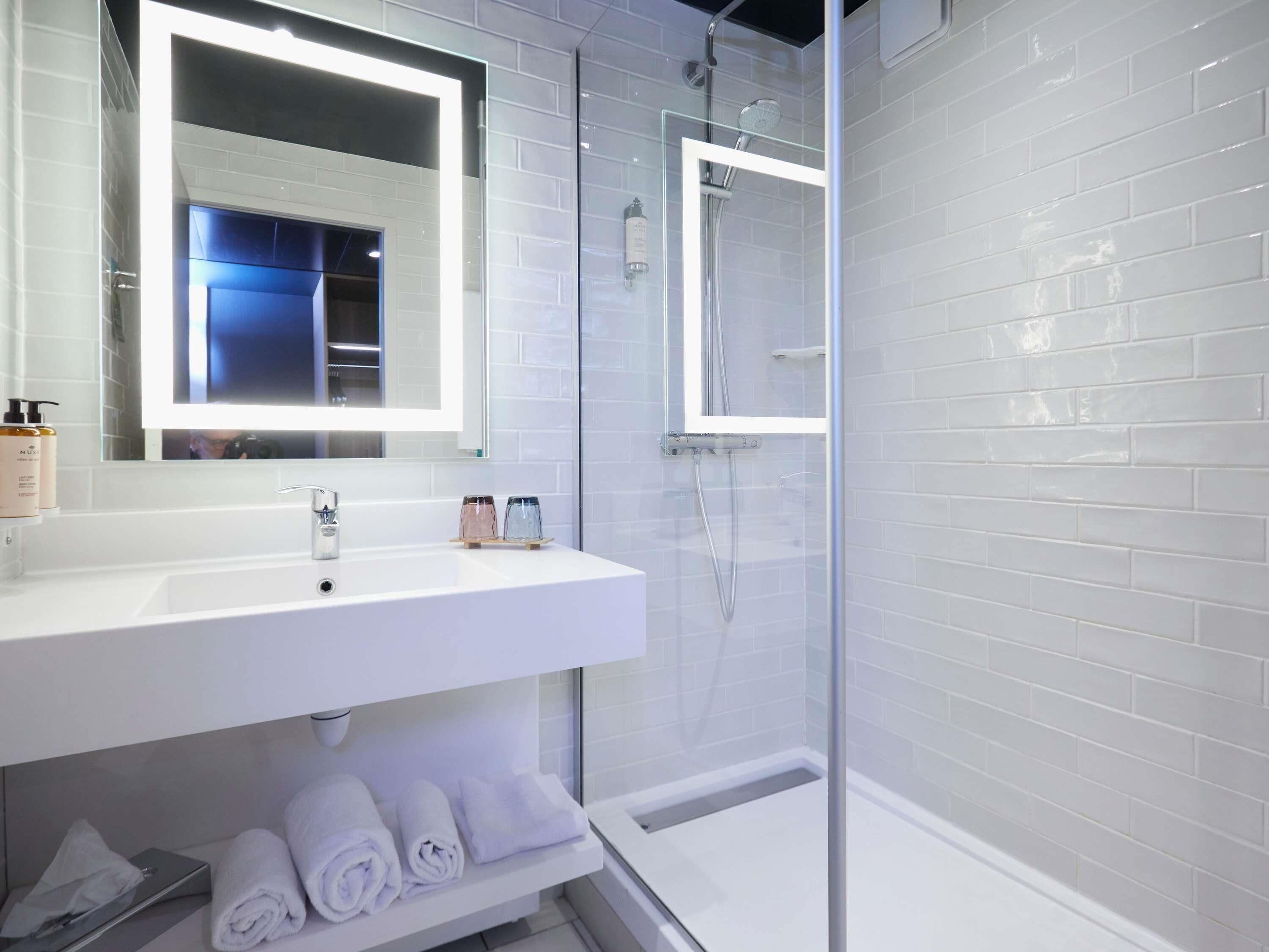 A modern bathroom with a white sink, mirror, and glass-enclosed shower.