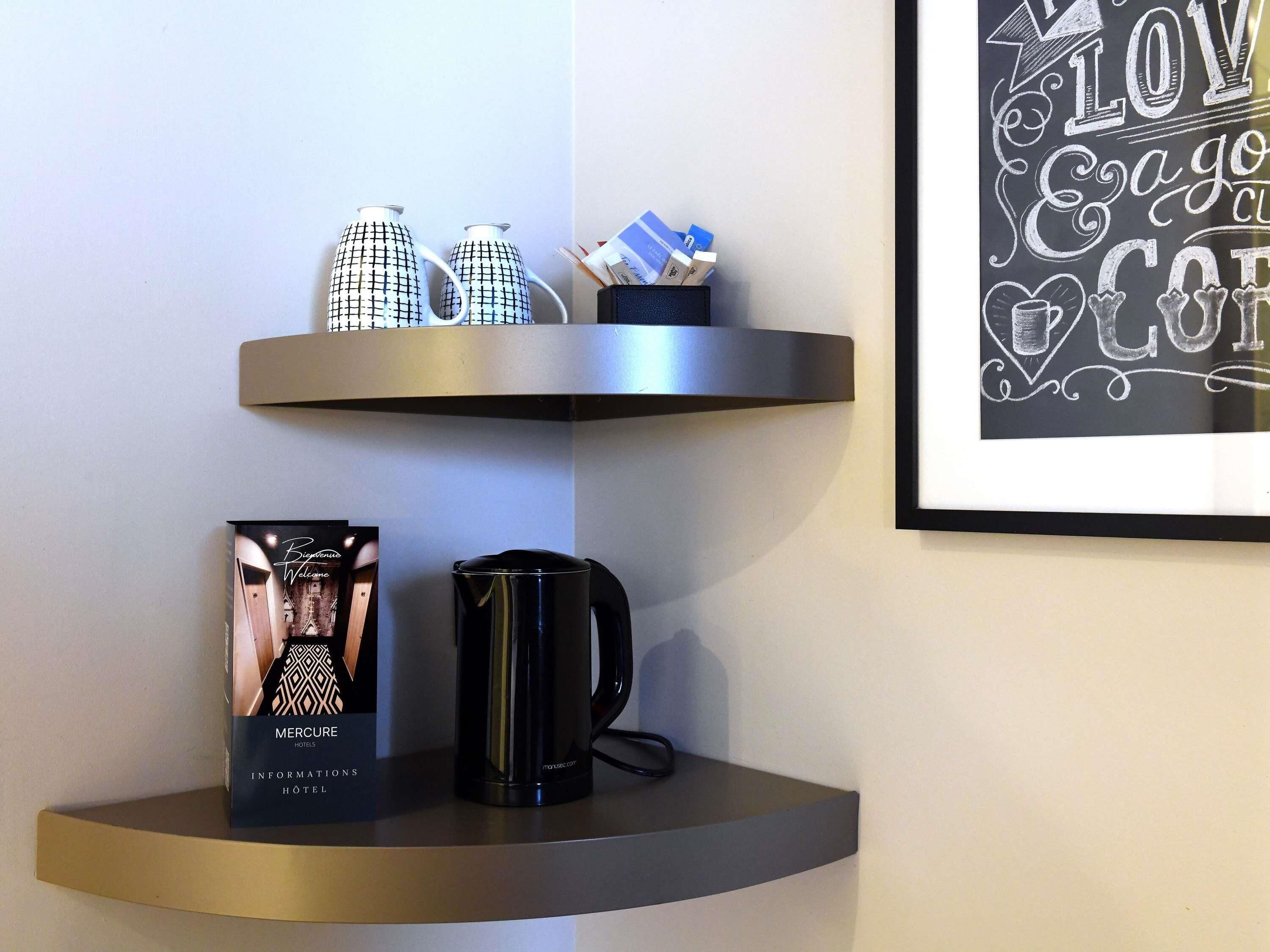 A wall-mounted shelf with a framed picture, a box of Mercure hotel information, and a black coffee maker.
