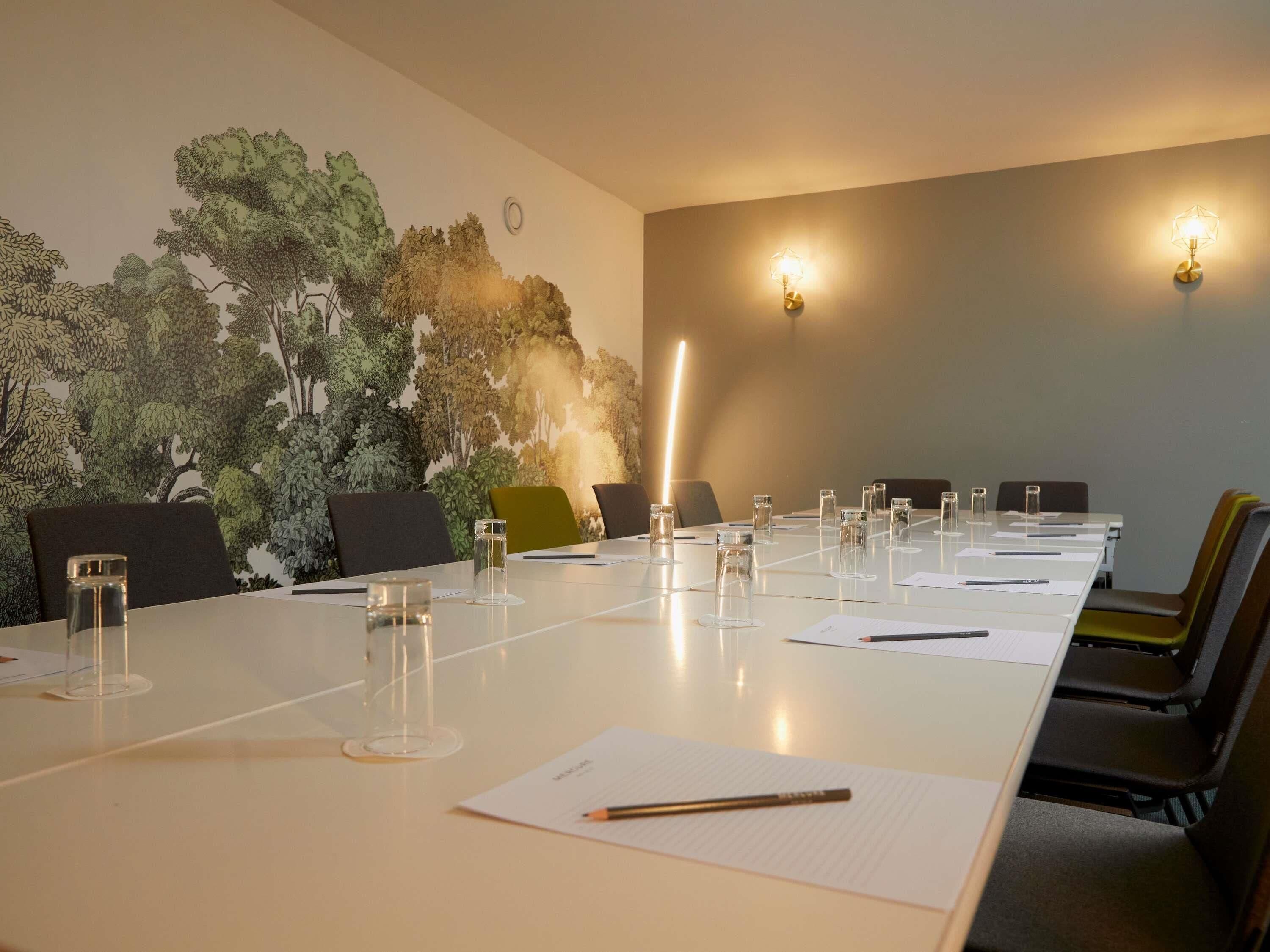 Un salón de conferencias con una larga mesa, sillas y un mural de árboles en la pared.