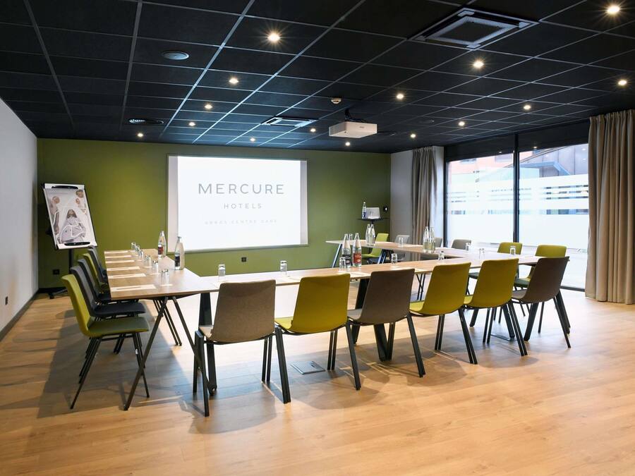 Un salón de conferencias con una larga mesa, sillas, una pantalla de proyector y una pizarra para presentaciones.