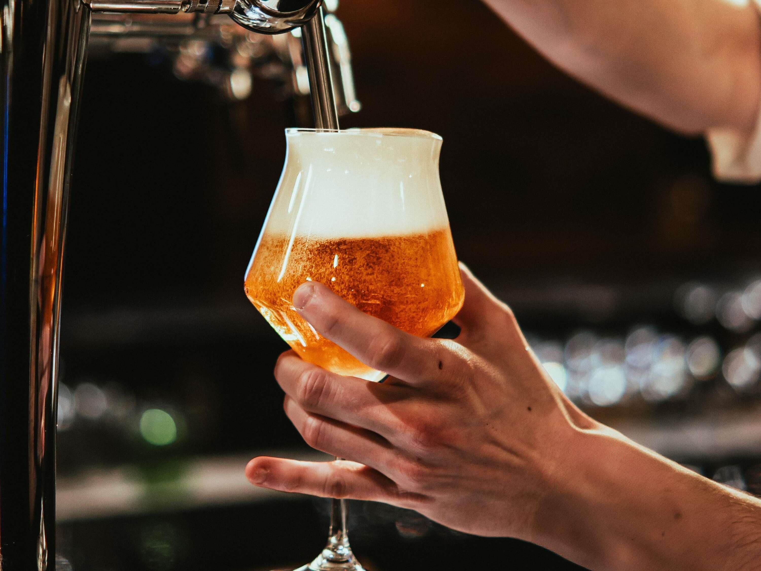 Una mano sostiene un vaso de cerveza que se está llenando desde un grifo.