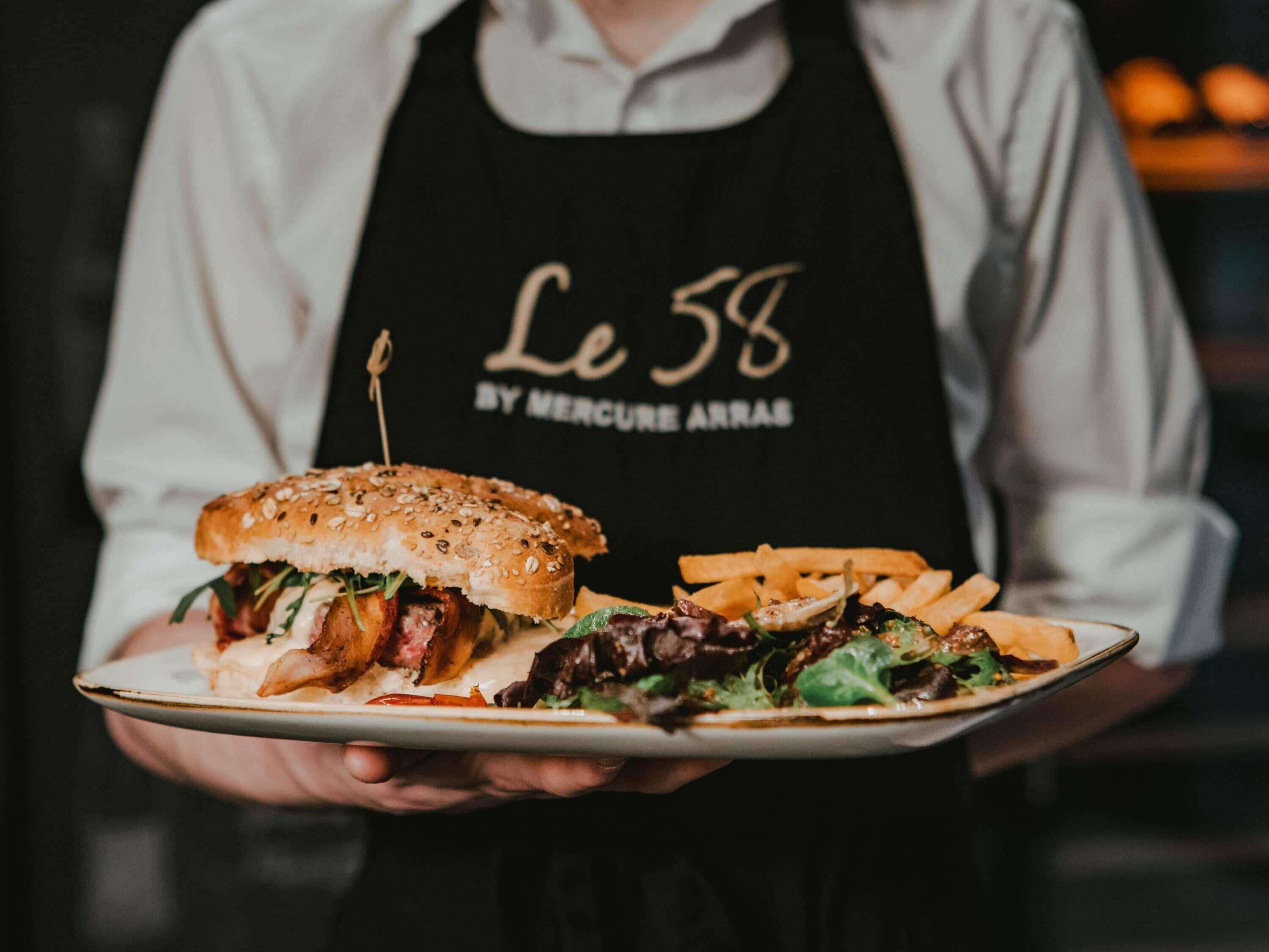 Una persona sosteniendo un plato con una hamburguesa, papas fritas y una ensalada.