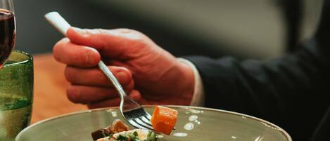 Una persona sosteniendo un tenedor sobre un bol de comida con verduras y un trozo de carne.