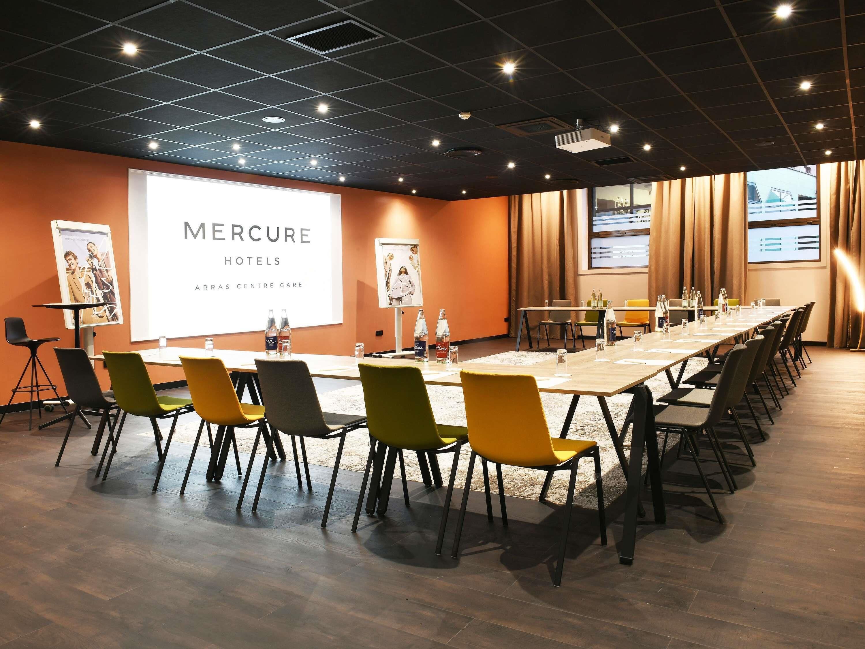 Un salón de conferencias con una larga mesa, sillas y pantallas de presentación en Mercure Hotels.