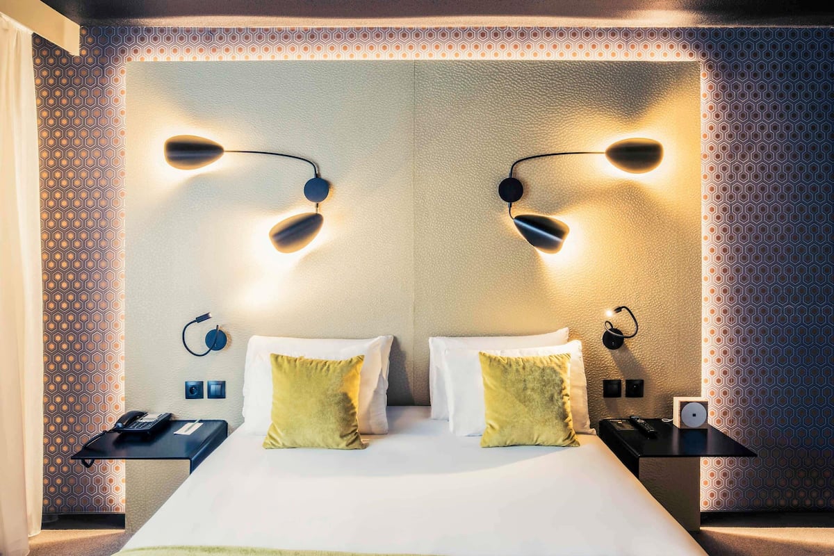 A hotel room with a large bed, two bedside tables, a phone, and a lamp on each table.