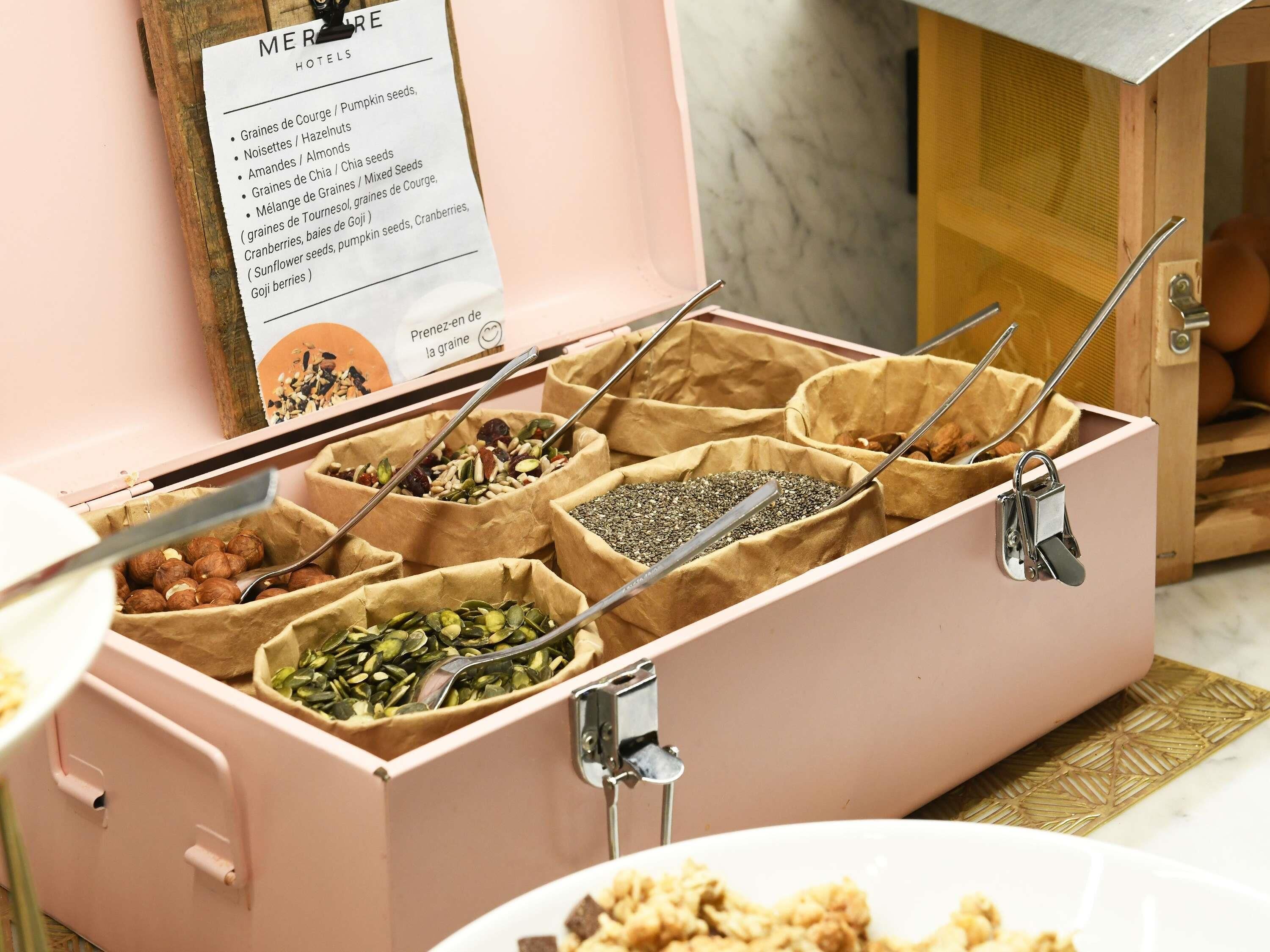 A pink storage box with multiple compartments containing various seeds and nuts.