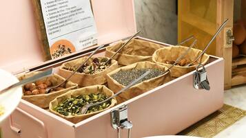 A pink storage box with multiple compartments containing various seeds and nuts.