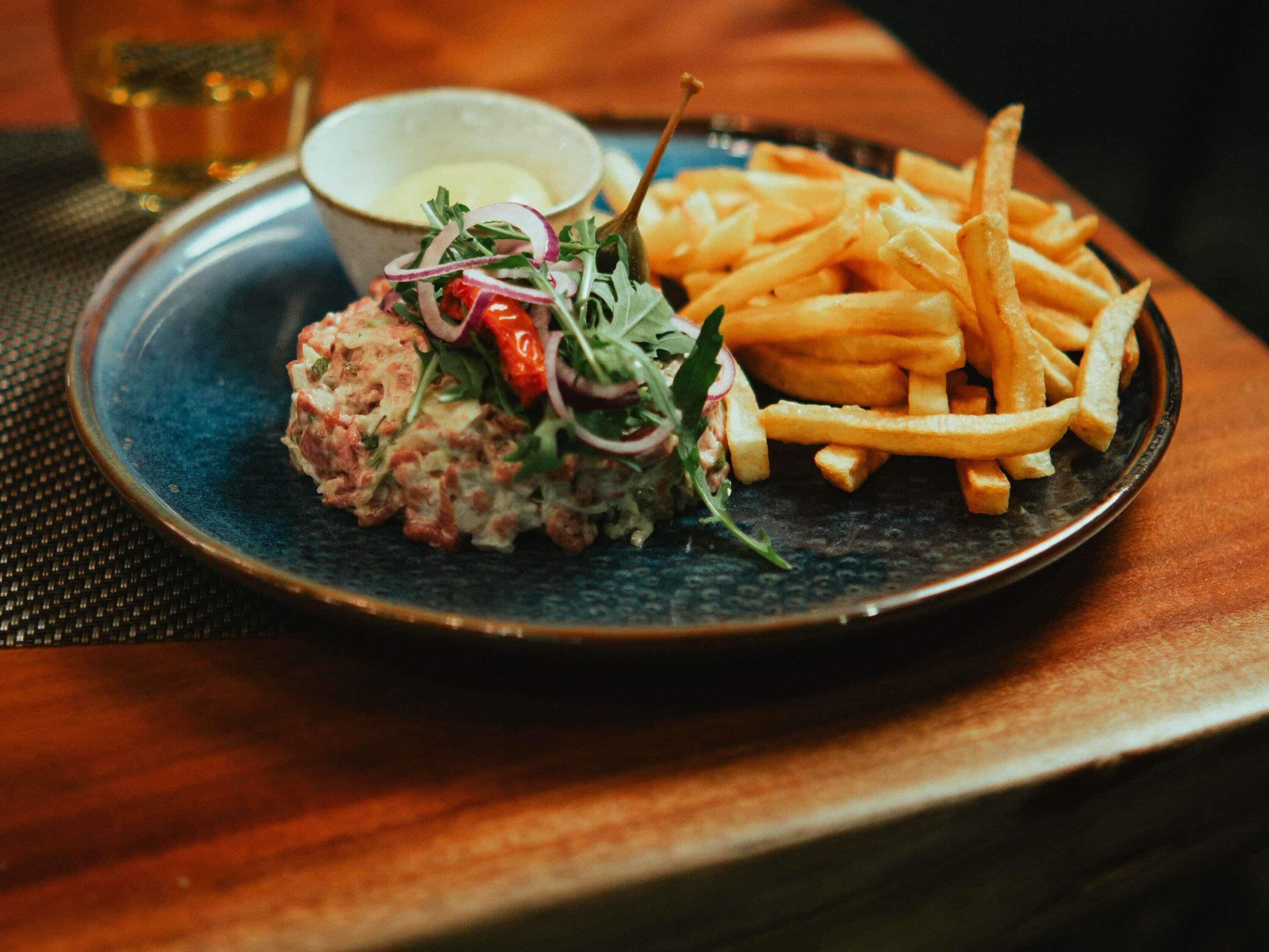 En tallrik med en köttbulle, pommes frites och en sallad, serverat på en mörk tallrik.