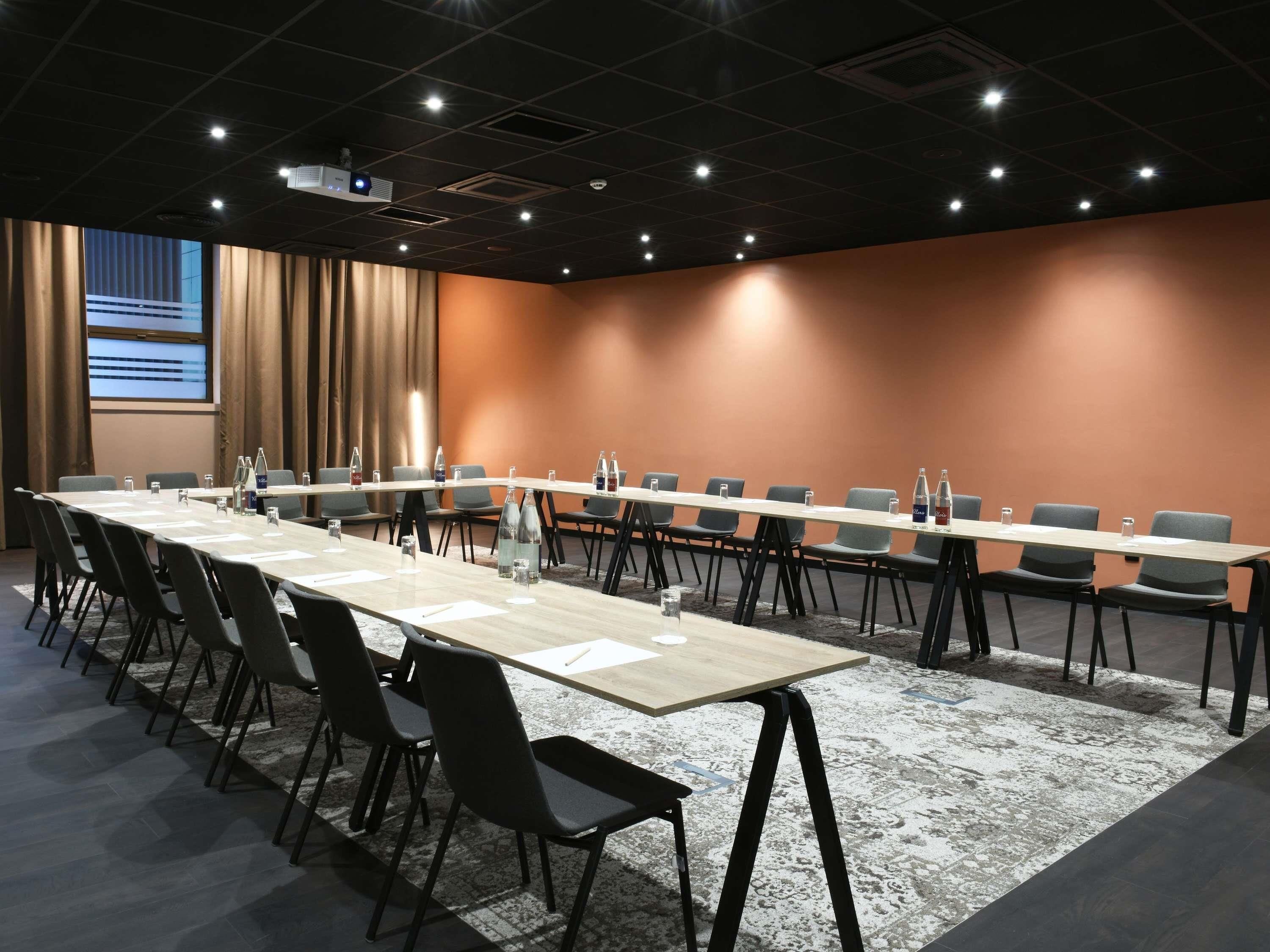 A conference room with a long table, chairs, a projector screen, and a large window.