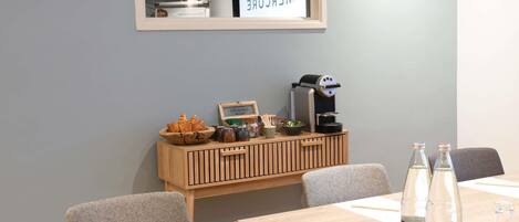 A conference room with a wooden table, chairs, a coffee machine, and a small display case with pastries.