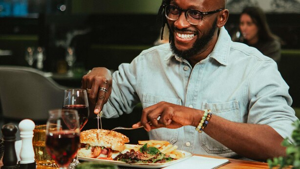 A person dining at a restaurant with a plate of food, a glass of red wine, and condiments on the table. - Mercure Arras Centre Gare (Arras)