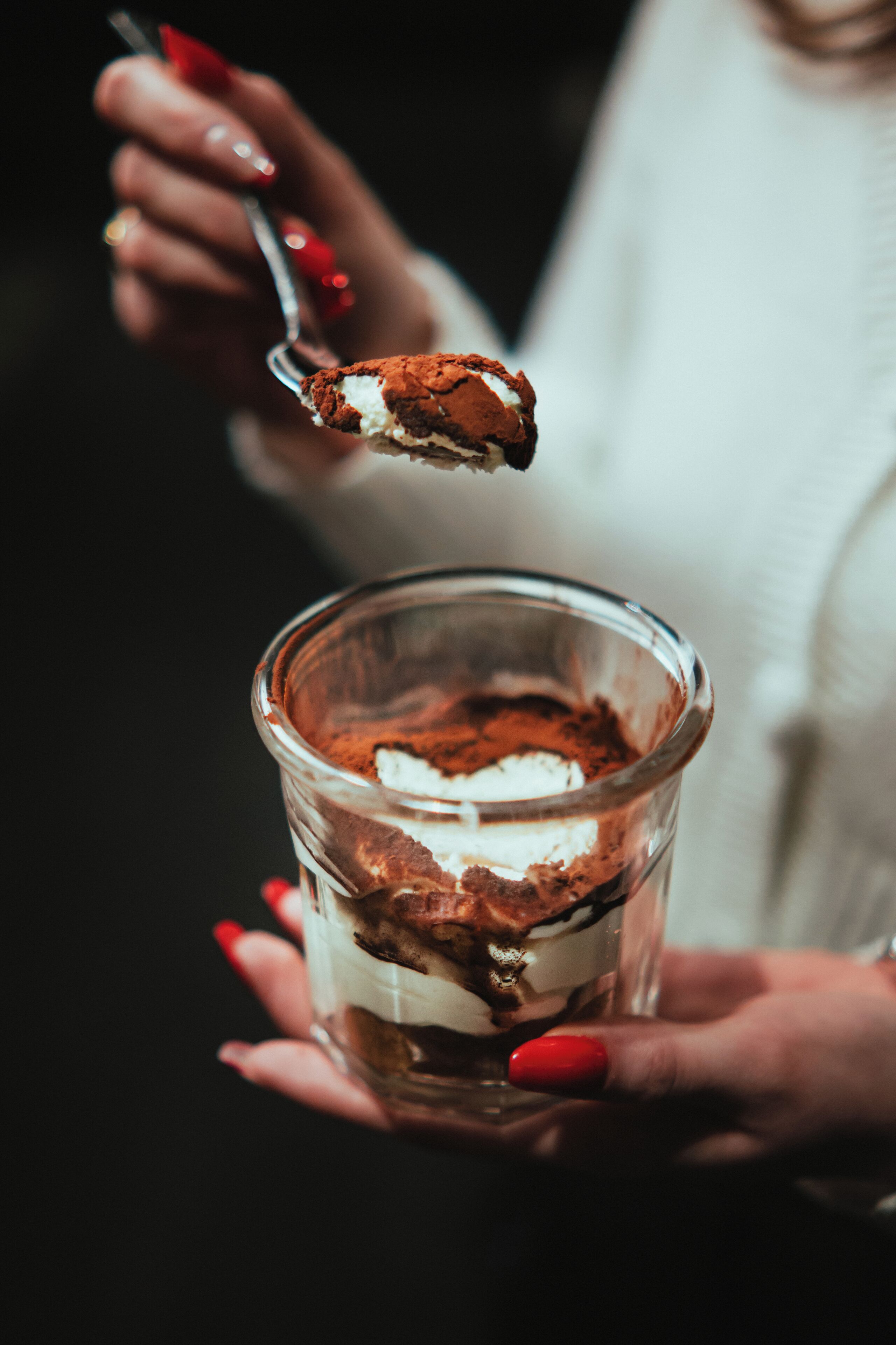 A person holding a glass with a layered dessert.